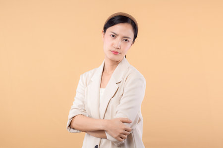 Studio portrait of successful happy confident young asian business woman. Beautiful young lady in white jacket smiling at camera standing isolated on solid beige colour copyspace backgroundの写真素材
