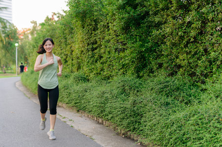 Fit young Asian woman jogging in park smiling happy running and enjoying a healthy outdoor...