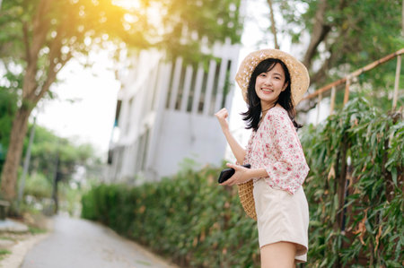 Portrait of young asian woman traveler with weaving hat and basket happy smile on green public park nature background. Journey trip lifestyle, world travel explorer or Asia summer tourism concept.の写真素材