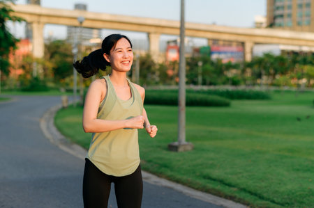 Fit young Asian woman jogging in park smiling happy running and enjoying a healthy outdoor lifestyle. Female jogger. Fitness runner girl in public park. healthy lifestyle and wellness being conceptの写真素材