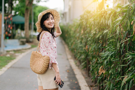 Portrait of young asian woman traveler with weaving hat and basket happy smile on green public park nature background. Journey trip lifestyle, world travel explorer or Asia summer tourism concept.の写真素材