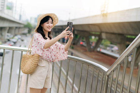 asian young woman traveler with weaving basket using mobile phone and standing on overpass with railway background. Journey trip lifestyle, world travel explorer or Asia summer tourism concept.の写真素材