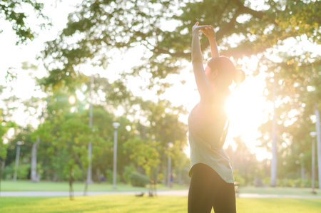 Female jogger. Fit Asian young woman with green sportswear stretching muscle in park before running and enjoying a healthy outdoor. Fitness runner girl in public park. Wellness being conceptの写真素材