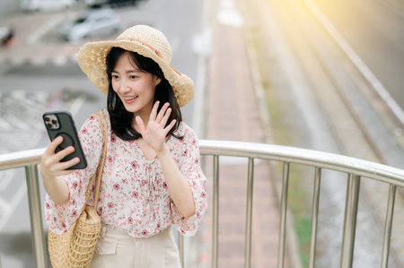 asian young woman traveler with weaving basket using mobile phone and standing on overpass with railway background. Journey trip lifestyle, world travel explorer or Asia summer tourism concept.の写真素材
