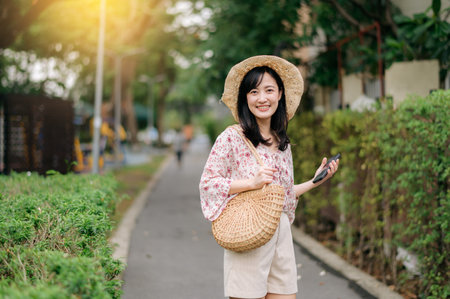 Portrait of young asian woman traveler with weaving hat and basket happy smile on green public park nature background. Journey trip lifestyle, world travel explorer or Asia summer tourism concept.の写真素材