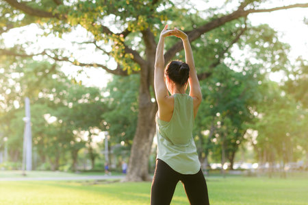 Female jogger. Fit Asian young woman with green sportswear stretching muscle in park before running and enjoying a healthy outdoor. Fitness runner girl in public park. Wellness being conceptの写真素材
