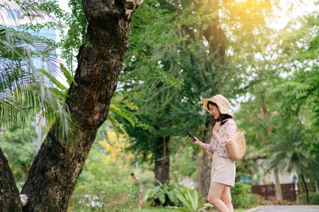 Portrait of young asian woman traveler with weaving hat and basket happy smile on green public park nature background. Journey trip lifestyle, world travel explorer or Asia summer tourism concept.の写真素材