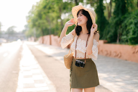 Portrait of young asian woman traveler with weaving hat and basket and a camera standing by the street. Journey trip lifestyle, world travel explorer or Asia summer tourism concept.の写真素材
