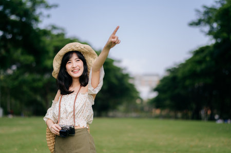 Portrait of young asian woman traveler with weaving hat and basket and a camera on green public park nature background. Journey trip lifestyle, world travel explorer or Asia summer tourism concept.の写真素材