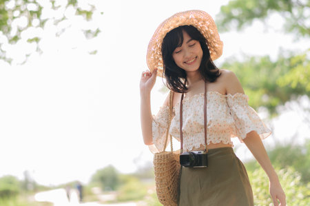 Portrait of young asian woman traveler with weaving hat and basket and a camera on green public park nature background. Journey trip lifestyle, world travel explorer or Asia summer tourism concept.の写真素材