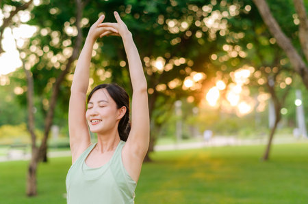 Female jogger. Fit Asian young woman with green sportswear stretching muscle in park before running and enjoying a healthy outdoor. Fitness runner girl in public park. Wellness being conceptの写真素材