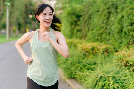 Fit young Asian woman jogging in park smiling happy running and enjoying a healthy outdoor lifestyle. Female jogger. Fitness runner girl in public park. healthy lifestyle and wellness being conceptの写真素材