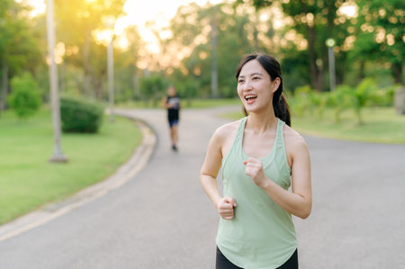 Fit young Asian woman jogging in park smiling happy running and enjoying a healthy outdoor lifestyle. Female jogger. Fitness runner girl in public park. healthy lifestyle and wellness being conceptの写真素材