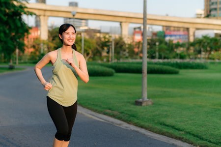 Fit young Asian woman jogging in park smiling happy running and enjoying a healthy outdoor lifestyle. Female jogger. Fitness runner girl in public park. healthy lifestyle and wellness being conceptの写真素材
