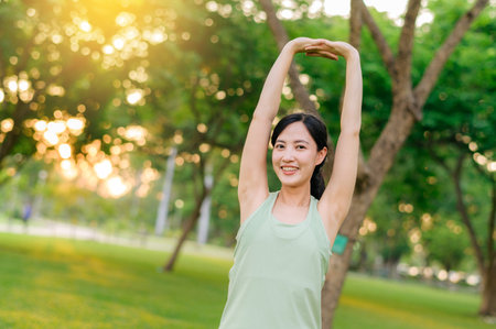 Female jogger. Fit Asian young woman with green sportswear stretching muscle in park before running and enjoying a healthy outdoor. Fitness runner girl in public park. Wellness being conceptの写真素材