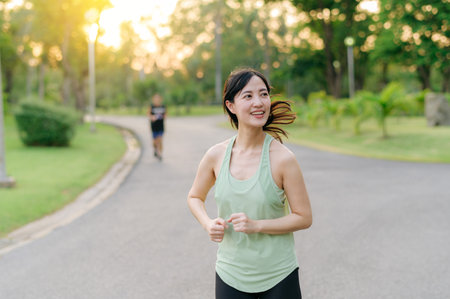 Fit young Asian woman jogging in park smiling happy running and enjoying a healthy outdoor lifestyle. Female jogger. Fitness runner girl in public park. healthy lifestyle and wellness being conceptの写真素材