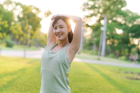 Female jogger. Fit Asian young woman with green sportswear stretching muscle in park before running and enjoying a healthy outdoor. Fitness runner girl in public park. Wellness being conceptの写真素材
