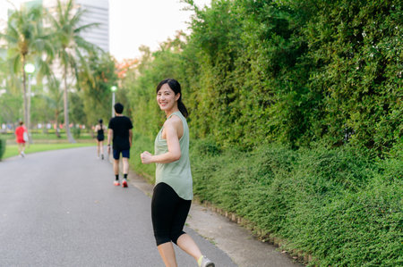 Fit young Asian woman jogging in park smiling happy running and enjoying a healthy outdoor lifestyle. Female jogger. Fitness runner girl in public park. healthy lifestyle and wellness being conceptの写真素材