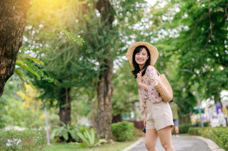 Portrait of young asian woman traveler with weaving hat and basket happy smile on green public park nature background. Journey trip lifestyle, world travel explorer or Asia summer tourism concept.の写真素材