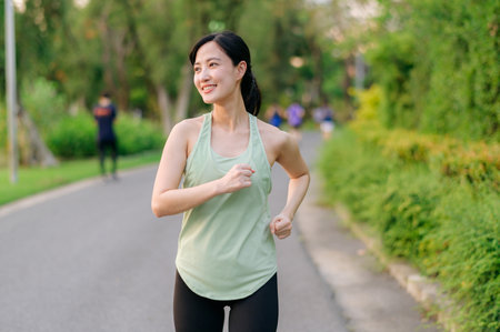 Fit young Asian woman jogging in park smiling happy running and enjoying a healthy outdoor lifestyle. Female jogger. Fitness runner girl in public park. healthy lifestyle and wellness being conceptの写真素材