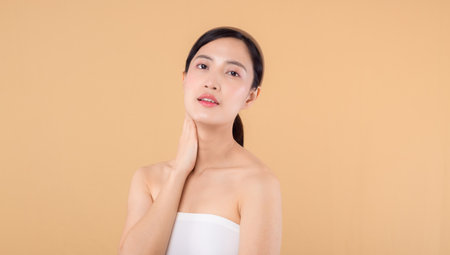 Beautiful asian girl model touching fresh glowing hydrated facial skin on beige background closeup. Beauty face young woman with natural makeup and healthy skin portrait. Skin care conceptの写真素材