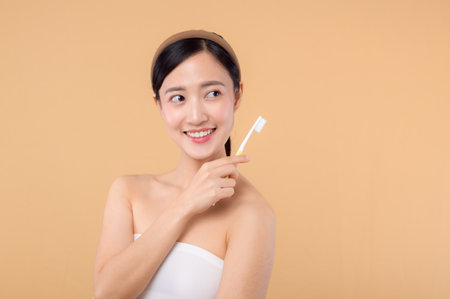 portrait young beauty woman with healthy happy smile holding toothbrush in her hand at morning isolated on beige studio background. hygiene tooth mouth clean care and dental concept.の写真素材