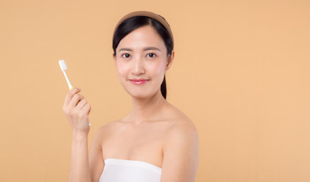 portrait young beauty woman with healthy happy smile holding toothbrush in her hand at morning isolated on beige studio background. hygiene tooth mouth clean care and dental concept.の写真素材