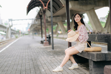asian young woman traveler with weaving basket waiting for train in train station. Journey trip lifestyle, world travel explorer or Asia summer tourism concept.の写真素材