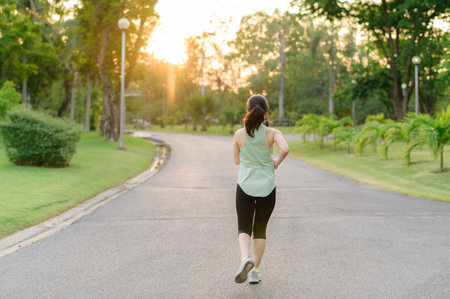 Fit young Asian woman jogging in park smiling happy running and enjoying a healthy outdoor lifestyle. Female jogger. Fitness runner girl in public park. healthy lifestyle and wellness being conceptの写真素材