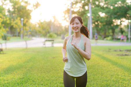 Fit young Asian woman jogging in park smiling happy running and enjoying a healthy outdoor lifestyle. Female jogger. Fitness runner girl in public park. healthy lifestyle and wellness being conceptの写真素材