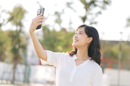 Portrait beautiful young asian woman with smart mobile phone around outdoor nature view in sunny summer dayの写真素材