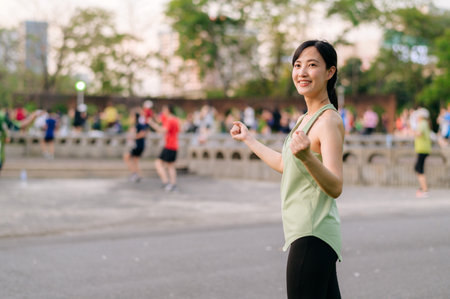Female jogger. Fit Asian young woman with green sportswear aerobics dance exercise in park and enjoying a healthy outdoor. Fitness runner girl in public park. Wellness being conceptの写真素材
