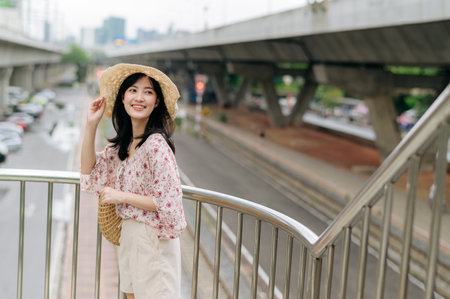 asian young woman traveler with weaving basket happy smiling standing on overpass with railway background. Journey trip lifestyle, world travel explorer or Asia summer tourism concept.の写真素材