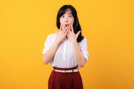 Portrait young beautiful asian woman enterpriser surprised face wearing white shirt and red plants isolated on yellow background.の写真素材