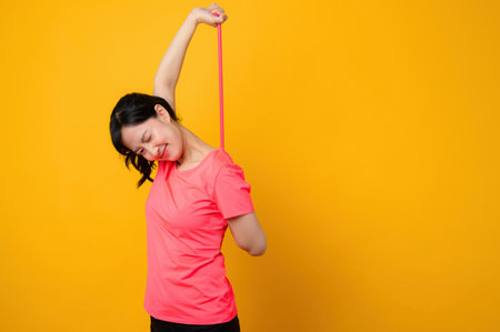 Portrait asian young sports fitness woman happy wearing pink sportswear and stretching resistance band doing exercise training workout against yellow background. wellbeing healthy lifestyle concept.の写真素材