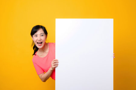 asian young sports fitness woman happy smile wearing pink sportswear standing behind the white blank banner or empty space advertisement board against yellow background. wellbeing lifestyle concept.の写真素材