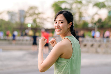Female jogger. Fit Asian young woman with green sportswear aerobics dance exercise in park and enjoying a healthy outdoor. Fitness runner girl in public park. Wellness being conceptの写真素材