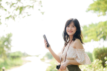 Portrait of young asian woman traveler with weaving hat, basket, mobile phone and camera on green public park background. Journey trip lifestyle, world travel explorer or Asia summer tourism concept.の写真素材