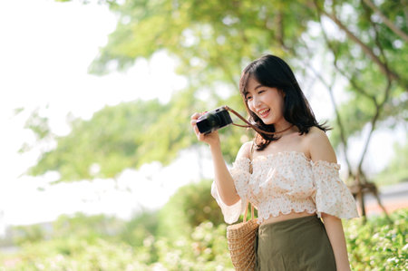 Portrait of young asian woman traveler with weaving hat and basket and a camera on green public park nature background. Journey trip lifestyle, world travel explorer or Asia summer tourism concept.の写真素材