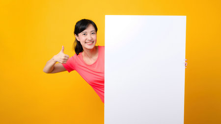 asian young sports fitness woman happy smile wearing pink sportswear standing behind the white blank banner or empty space advertisement board against yellow background. wellbeing lifestyle concept.の写真素材