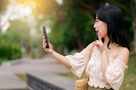 Portrait of young asian woman traveler with weaving hat, basket, mobile phone and camera on green public park background. Journey trip lifestyle, world travel explorer or Asia summer tourism concept.の写真素材