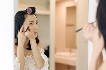 Beautiful Asian young woman applying makeup in front of the mirror. Lifestyle people concept. Advertisement for skin cream, anti-wrinkle cream, baby faceの写真素材