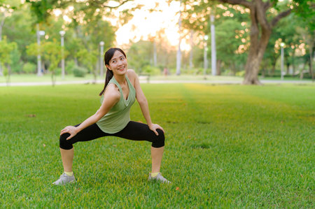 Female jogger. Fit Asian young woman with green sportswear stretching muscle in park before running and enjoying a healthy outdoor. Fitness runner girl in public park. Wellness being conceptの写真素材