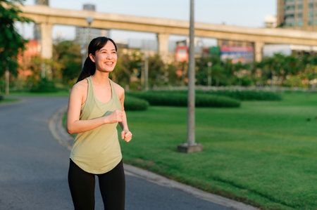 Fit young Asian woman jogging in park smiling happy running and enjoying a healthy outdoor lifestyle. Female jogger. Fitness runner girl in public park. healthy lifestyle and wellness being conceptの写真素材