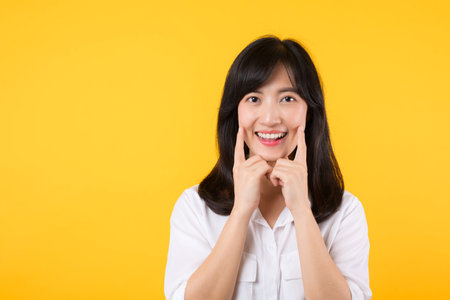 Young asian beautiful woman happy smile wearing white shirt and denim jean plants over yellow isolated background smiling confident showing and pointing with fingers teeth and mouth. Dental concept.の写真素材