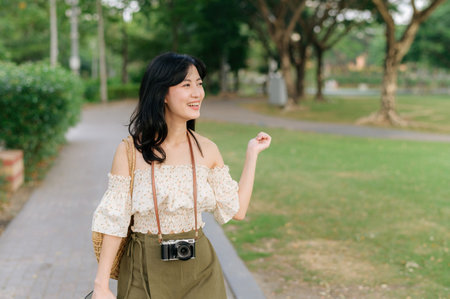 Portrait of young asian woman traveler with weaving hat and basket and a camera on green public park...