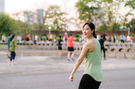 Female jogger. Fit Asian young woman with green sportswear aerobics dance exercise in park and enjoying a healthy outdoor. Fitness runner girl in public park. Wellness being conceptの写真素材