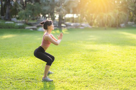 Healthy outdoor lifestyle with fit Asian young woman 30s wearing pink sportswear squat muscles in public park before going for invigorating run, embodying the wellness concept.の写真素材
