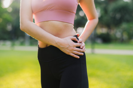 Close up fit female jogger as an Asian woman 30s, wearing pink sportswear, warms down and holds hip after a sunset run in a public park. Embrace the concept of wellness living and nature.の写真素材