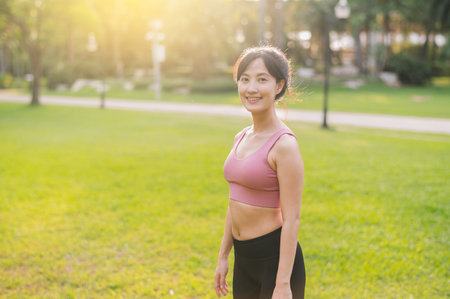 Experience the joy of a happy, fit 30s female jogger. Asian woman wearing pink sportswear, enjoying fresh air in a public park. Embrace wellness living and connect with nature.の写真素材